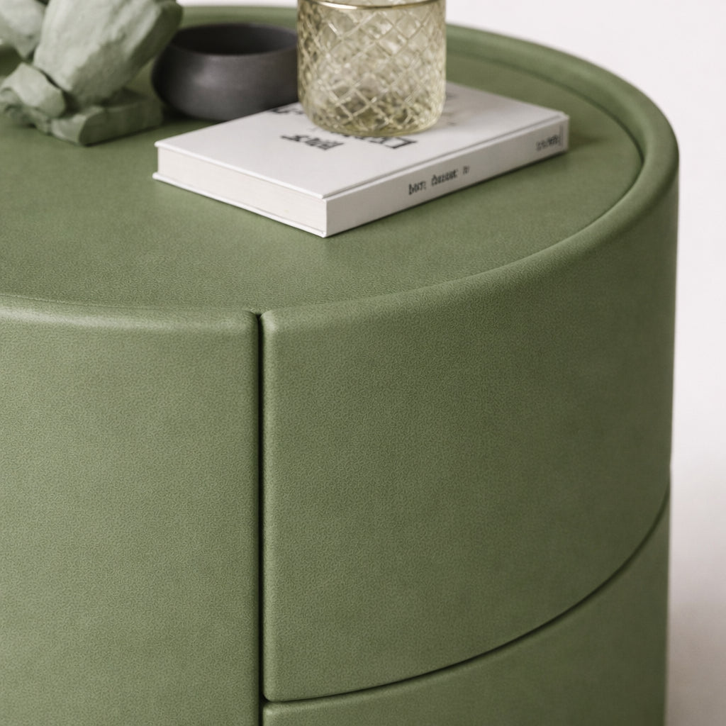 Green cylindrical side table with a book and decorative items on top