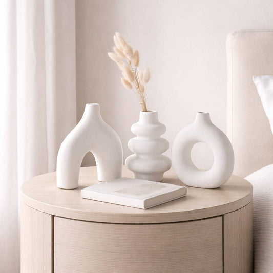 Three white ceramic vases on a wooden side table with a neutral background
