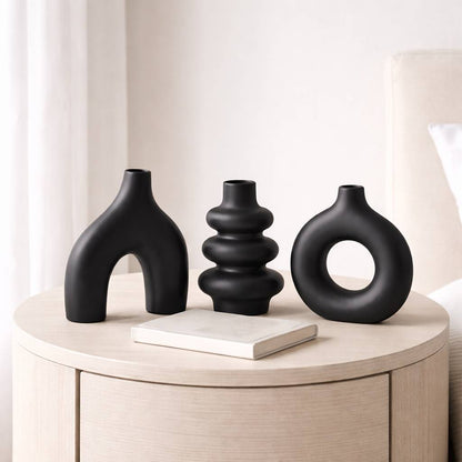 Three black vases on a wooden surface with a neutral background