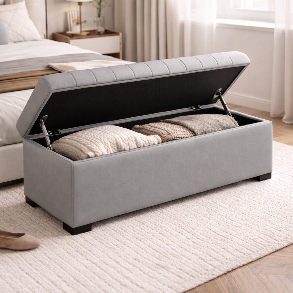 Gray storage ottoman with open lid revealing cushions in a bedroom setting.