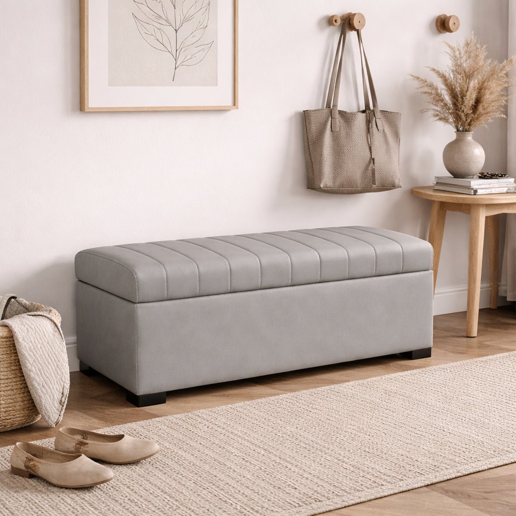 Gray storage bench in a room with a rug, shoes, and wall art.