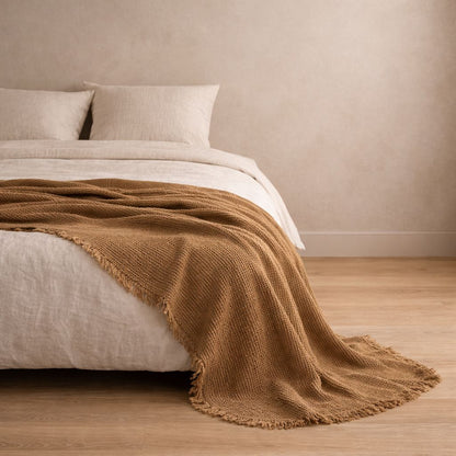 Bed with brown blanket and white bedding against a beige wall.