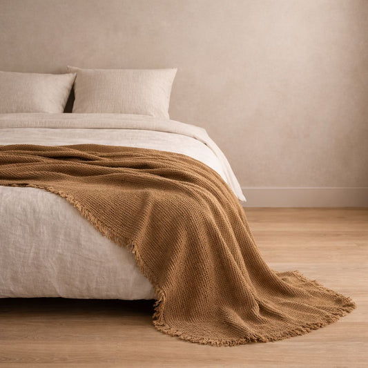 Bed with brown blanket and white bedding against a beige wall.