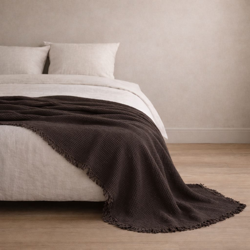 Brown blanket draped over a bed in a minimalistic room with neutral walls and flooring.